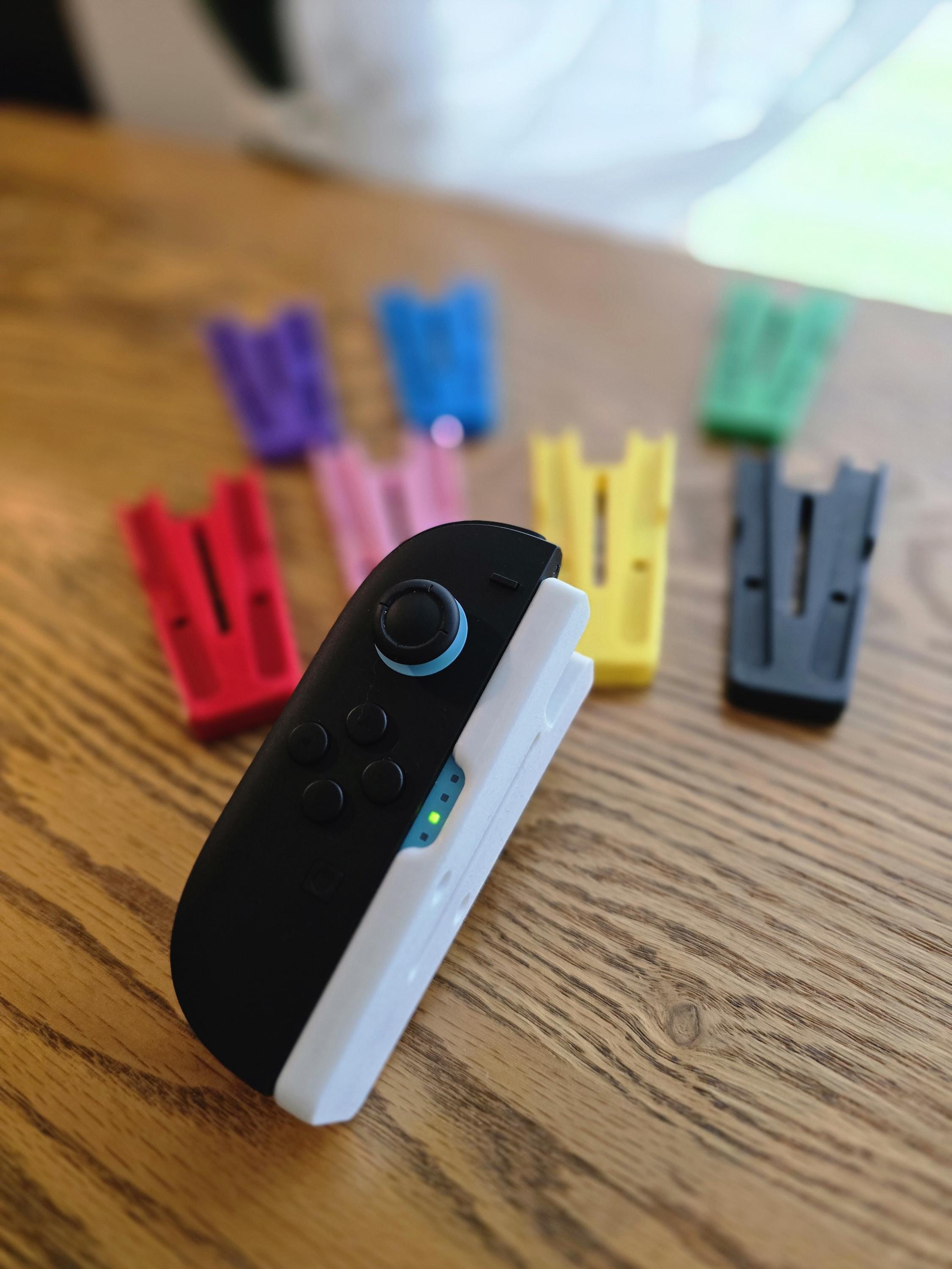 A black and white game controller is placed on a wooden surface, surrounded by various colored plastic clips.