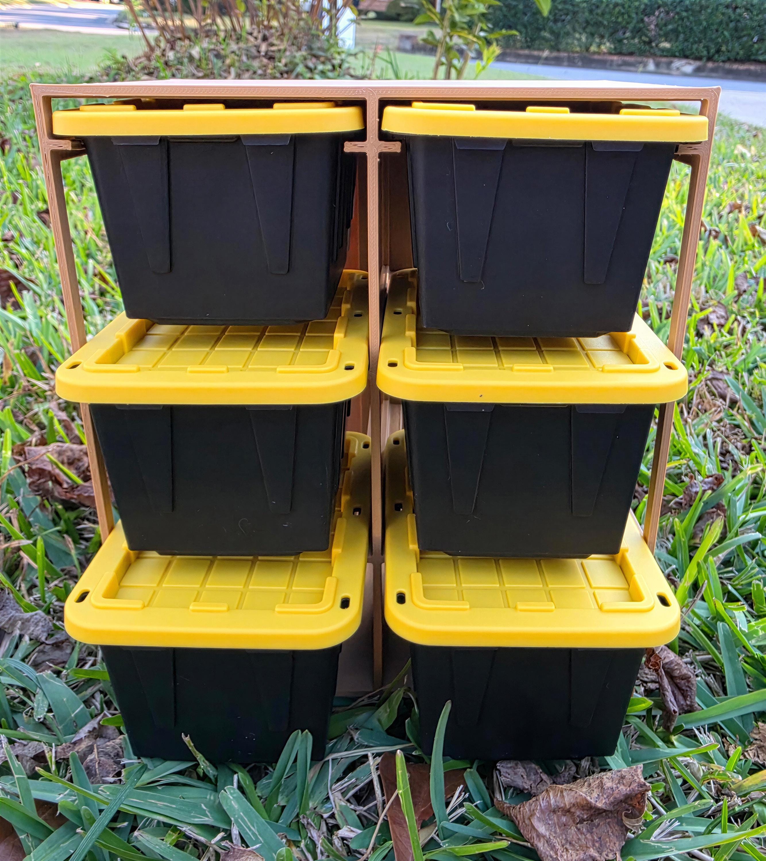 A stack of six black plastic storage bins with yellow lids, placed on a grassy lawn.