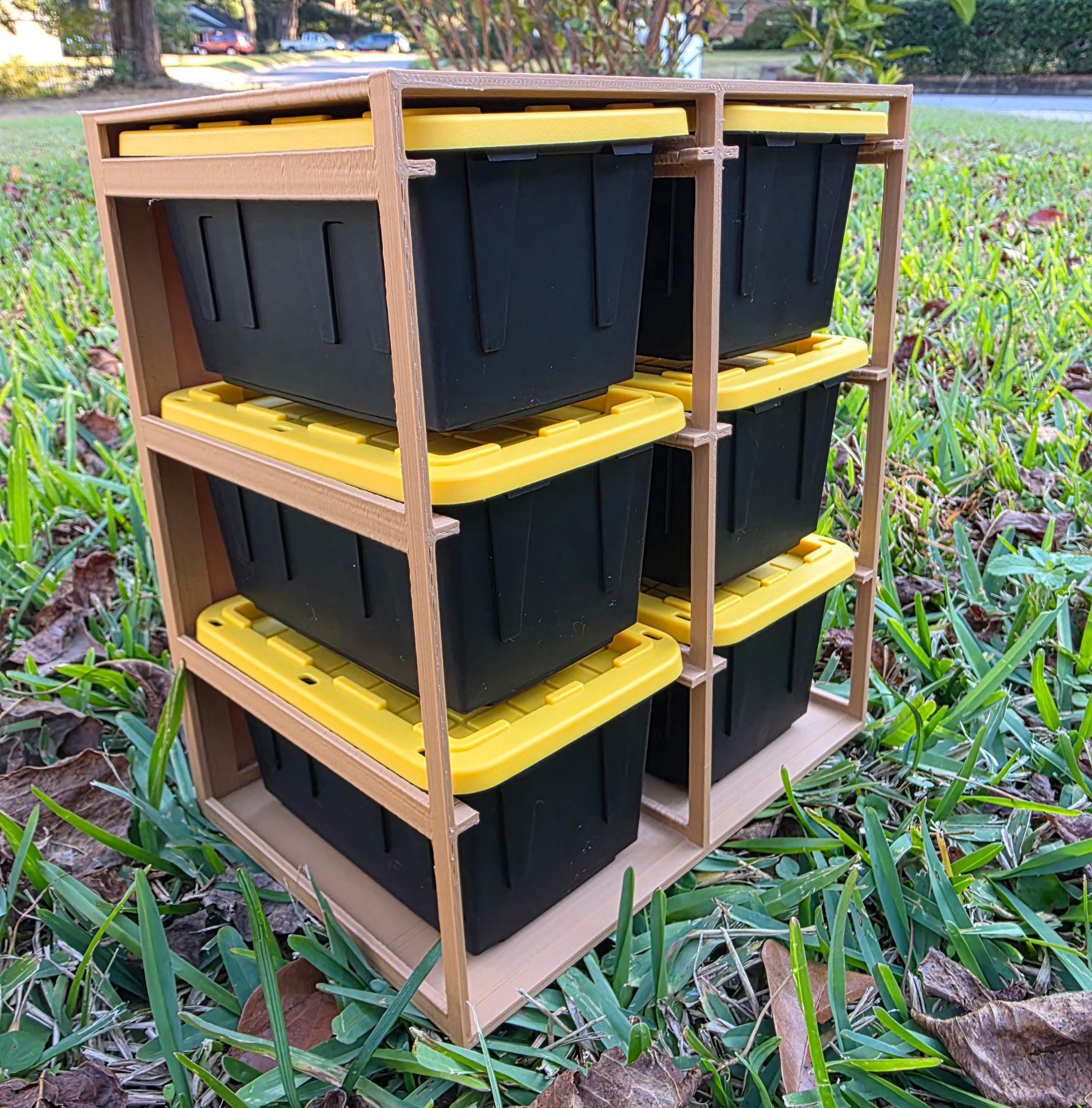A wooden storage unit with six black plastic storage bins stacked on top of each other, placed on a grassy lawn.
