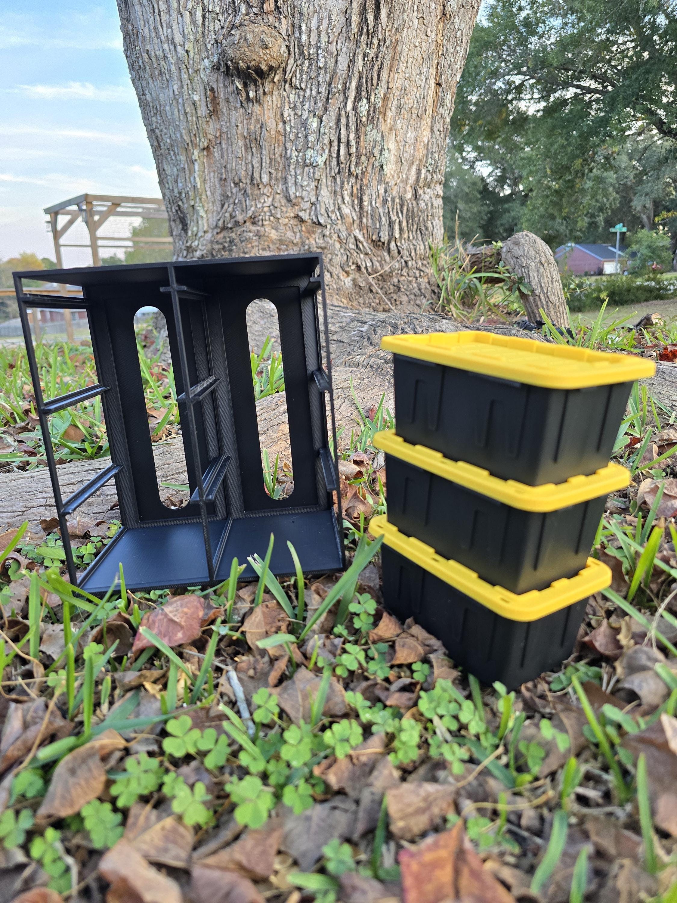 a black metal structure with three yellow plastic containers stacked on top of it, placed on the ground near a tree trunk.