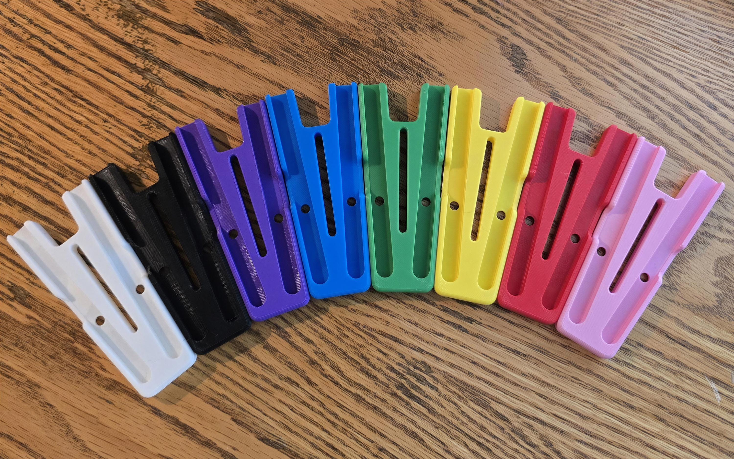 A collection of colorful plastic holders or holders in various colors, including white, black, purple, green, yellow, pink, and red, arranged in a row on a wooden surface.