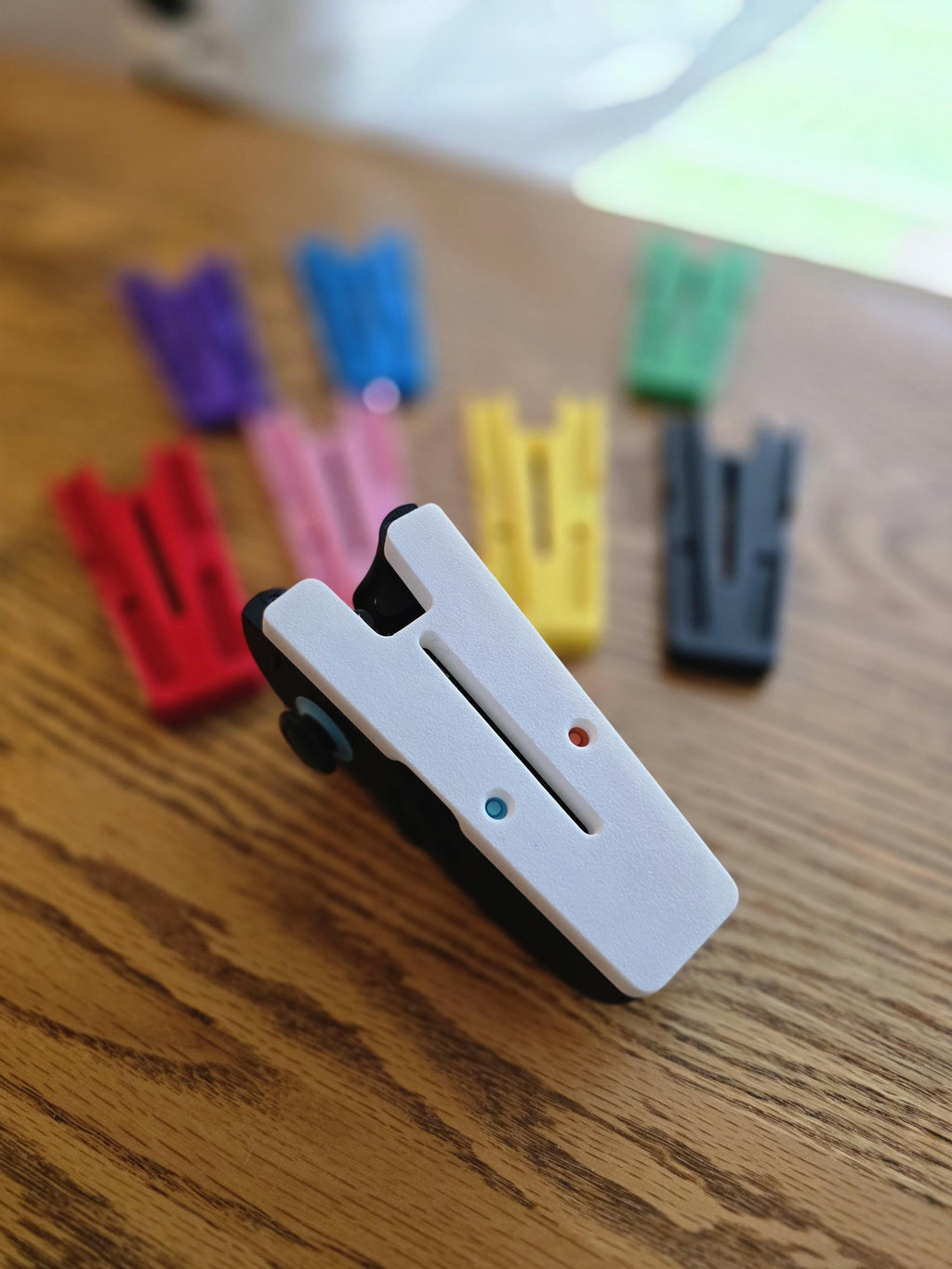 a white plastic clip with two blue and red buttons, surrounded by various colored plastic clips on a wooden surface.