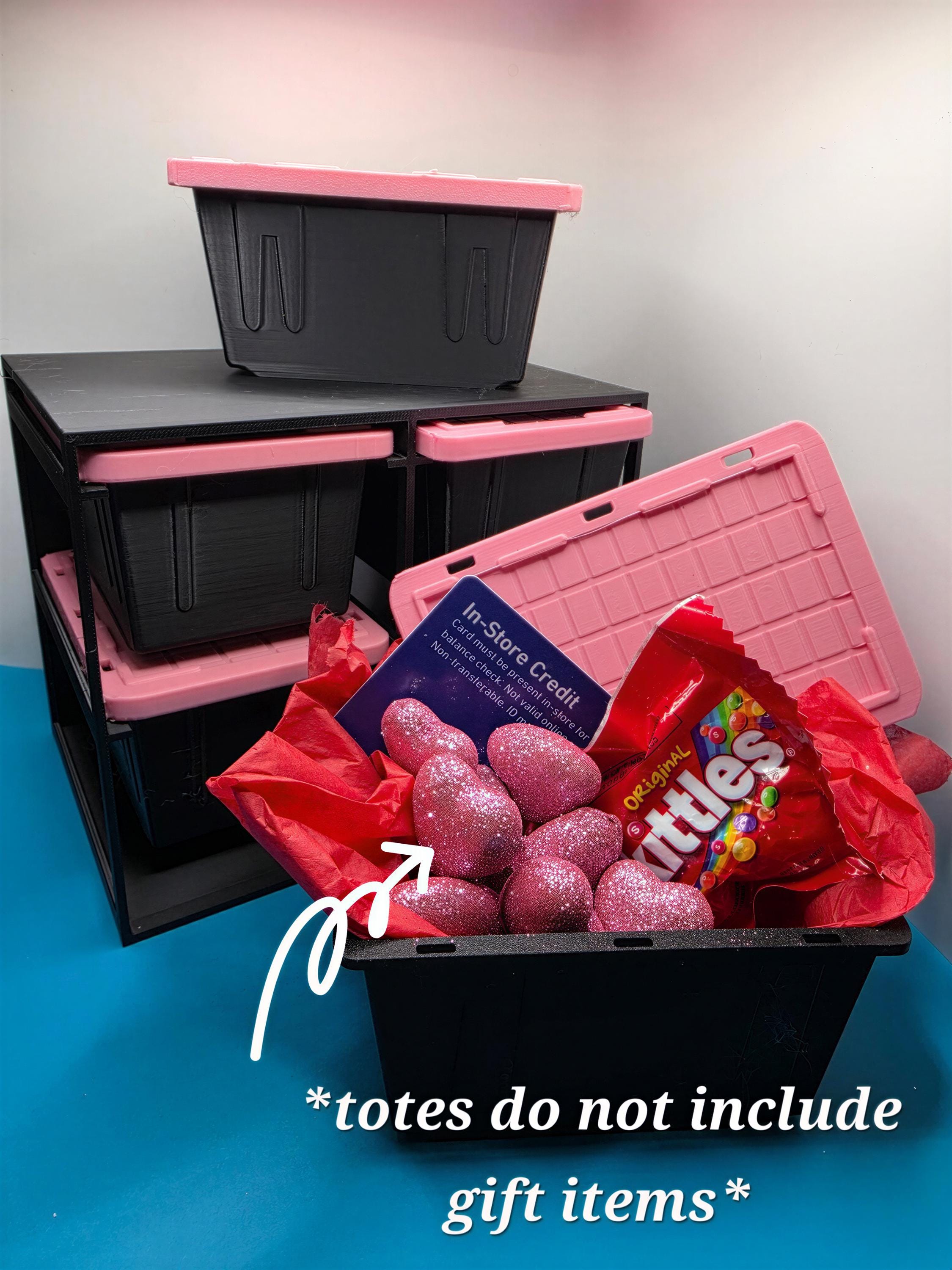 A pink storage bin filled with various items, including a bag of candy, a pink bag, and some pink glittery objects, with a black storage bin and pink storage bin stacked on top.