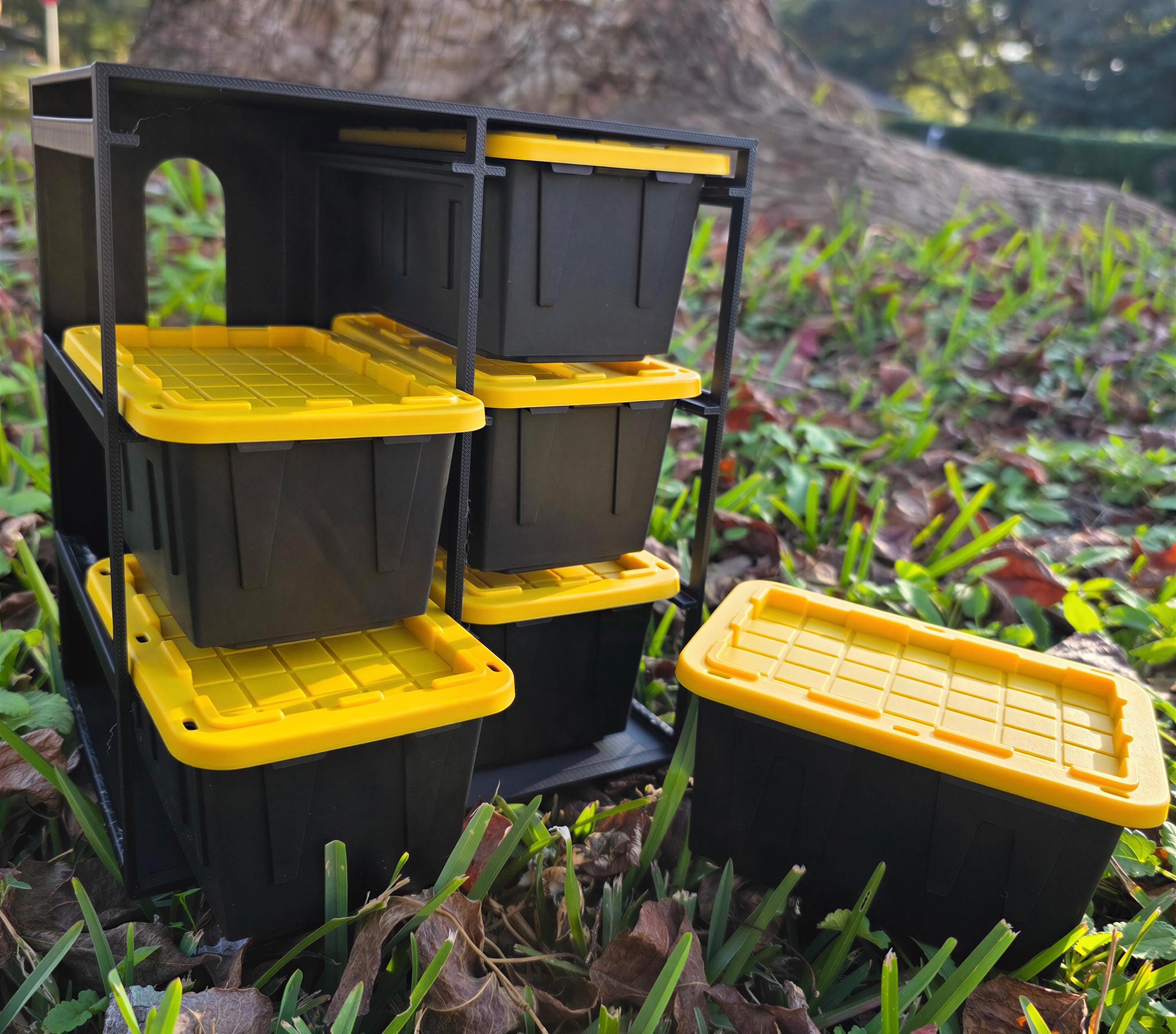 A set of black and yellow storage containers is placed on the ground in a grassy area, with a tree trunk visible in the background.