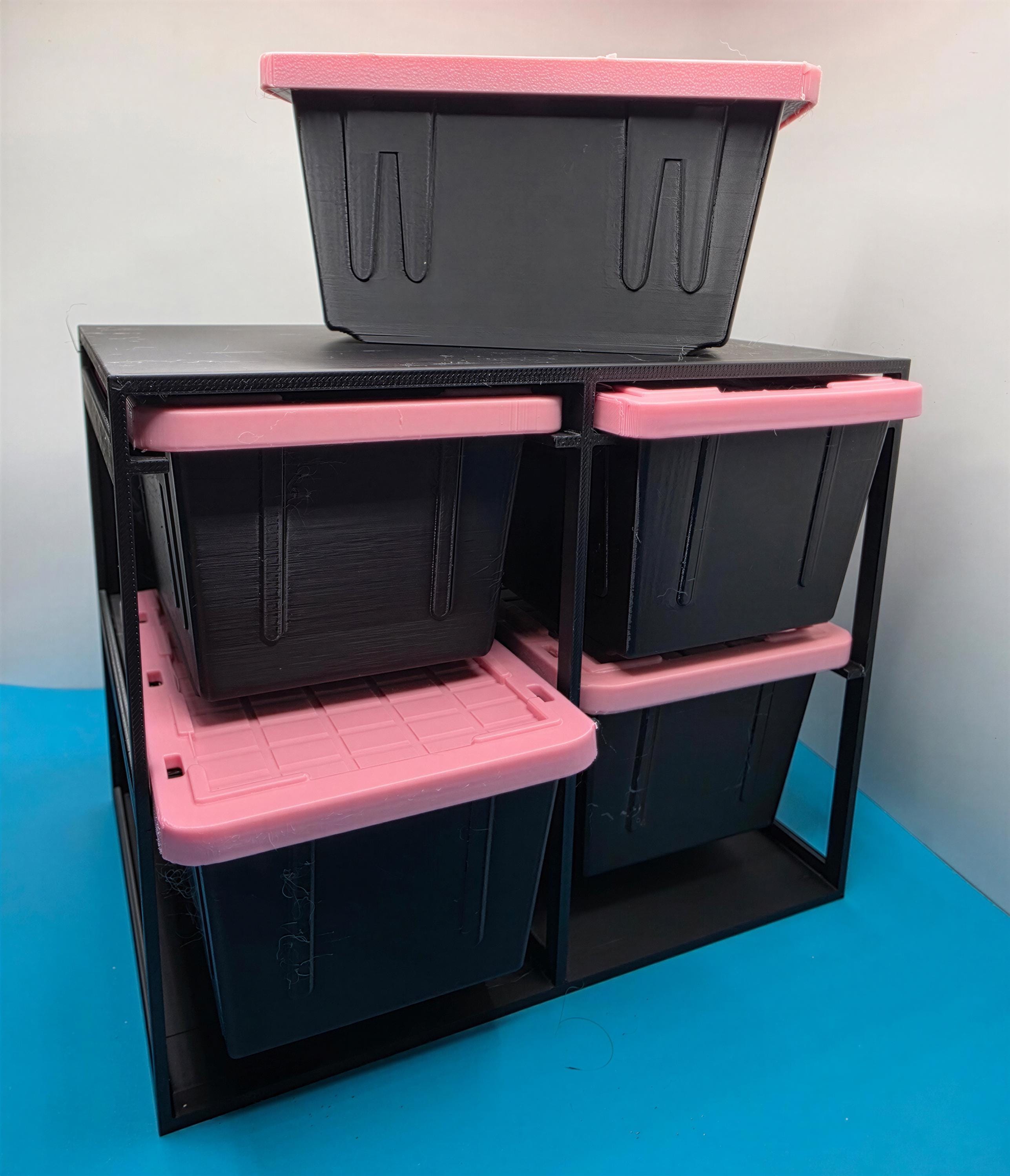 A storage unit with multiple black plastic bins stacked on top of each other, with pink plastic bins on the bottom.